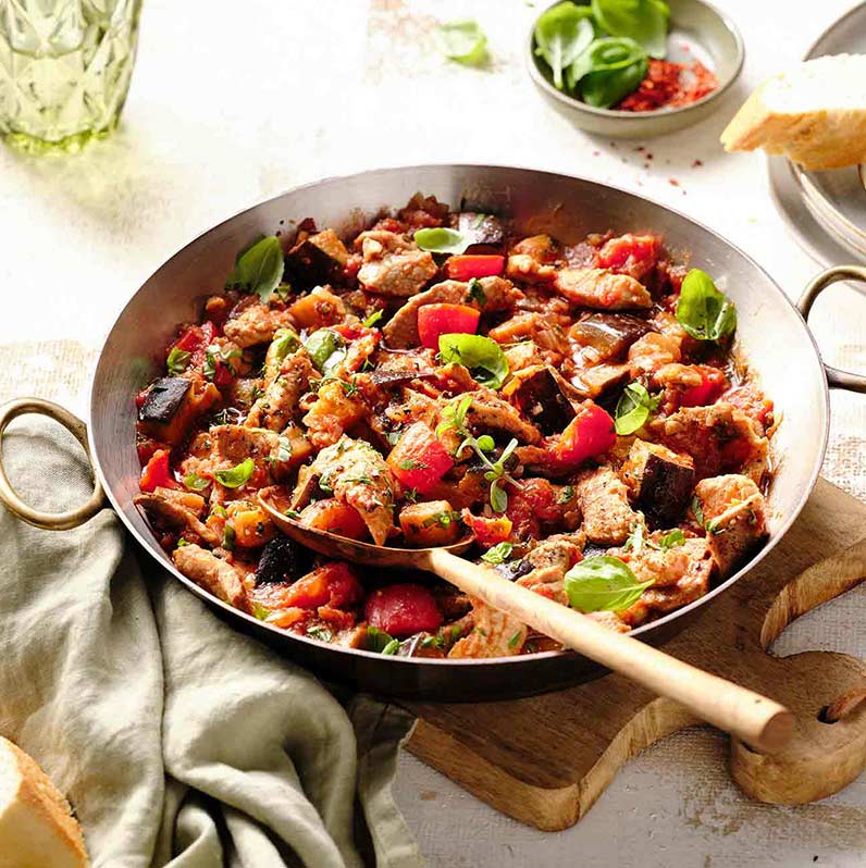 In einer großen Pfanne serviertes mediterranes Schweinegeschnetzeltes, dekoriert mit buntem Gemüse und Kräutern.