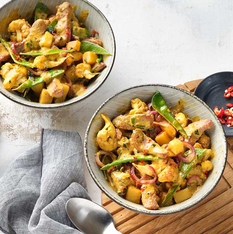 Zwei Schalen mit Puten-Curry, die aromatisch gewürzt sind und mit frischen Zutaten angerichtet wurden.