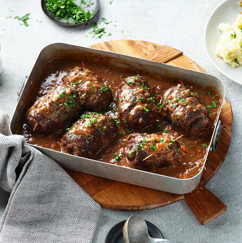 Rinderroulade im Bräter, zart und saftig, umgeben von aromatischem Gemüse und einer köstlichen Soße.
