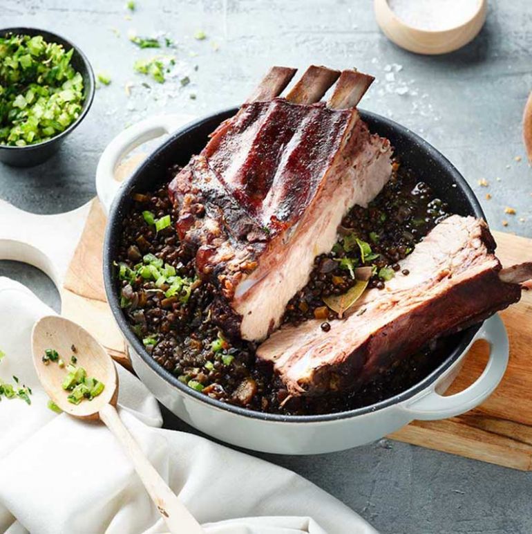 Dicke Schweinerippe in einem Topf, zart gegart und bereit zum Servieren, umgeben von aromatischen Kräutern.