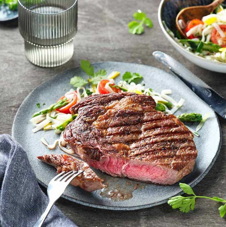 Ein saftiges Rib-Eye-Steak auf einem hellgrauem Teller, perfekt gegrillt und appetitlich angerichtet.